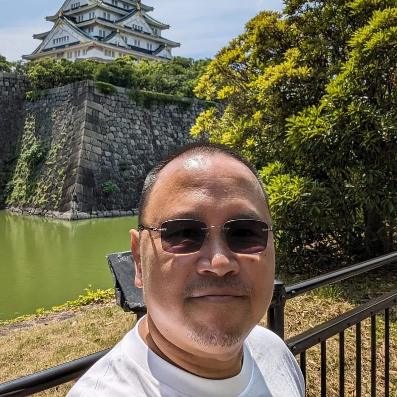 Man in sunglasses taking a selfie with Osaka Castle behind him in Osaka, Japan.