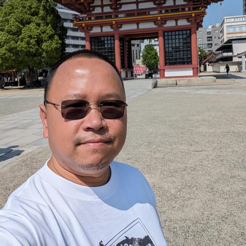 Man taking a selfie in front of the red gate at Shitennoji Temple in Osaka, Japan.