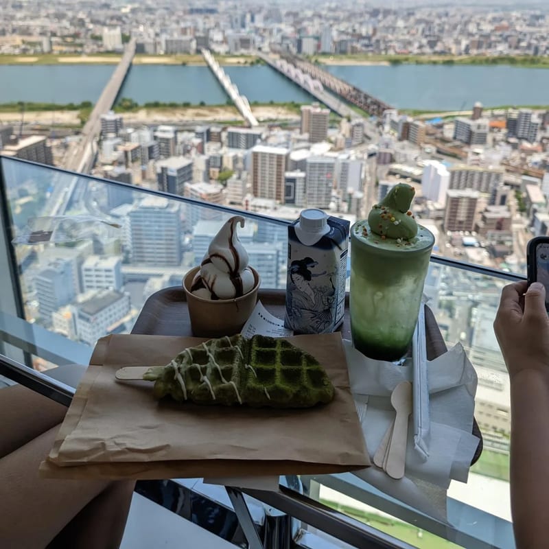 Matcha cream soda and matcha croffle desserts on a table with Osaka city view through window, Japan.