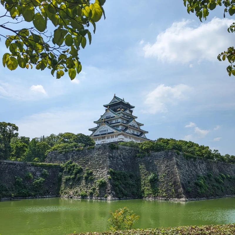 Osaka Castle main tower framed by green trees with moat in the foreground in Osaka, Japan.