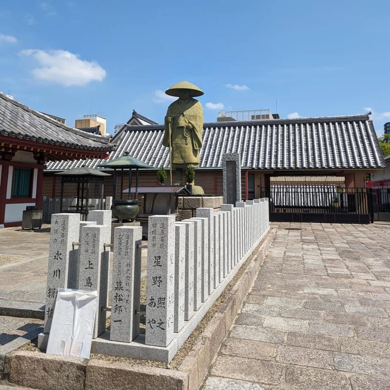 Stone statue of robed figure with conical hat in courtyard at Shitennoji Temple in Osaka, Japan.