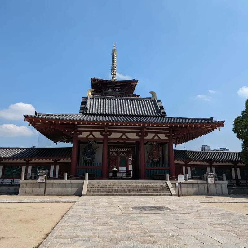 Main hall of Shitennoji Temple with golden spire and guardian statues under blue sky in Osaka, Japan.