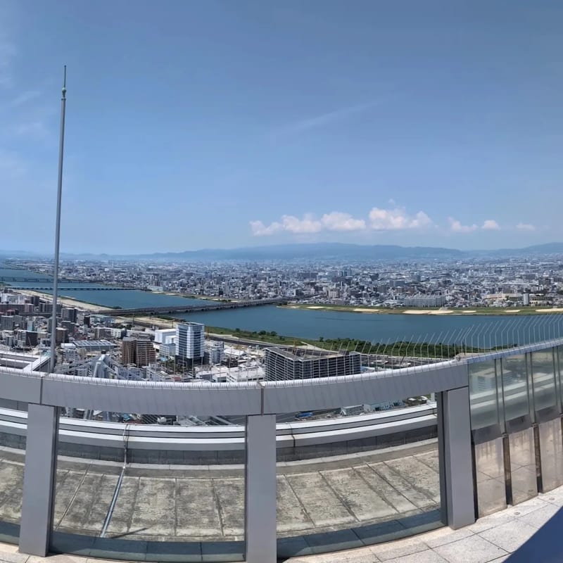 Sweeping panoramic view of Osaka, Japan from the open-air rooftop of the Umeda Sky Building, showing rivers, bridges, and the city skyline.