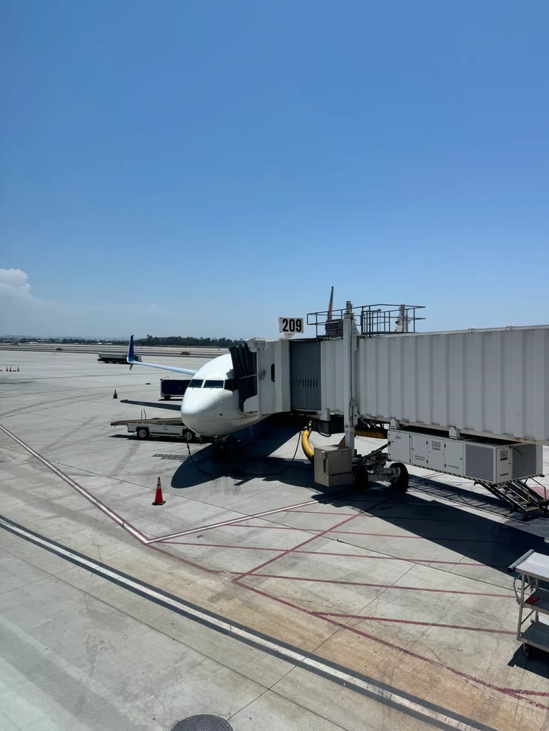 Delta airplane parked at Gate 209 at Ontario International Airport, California, connected to jet bridge under clear blue sky