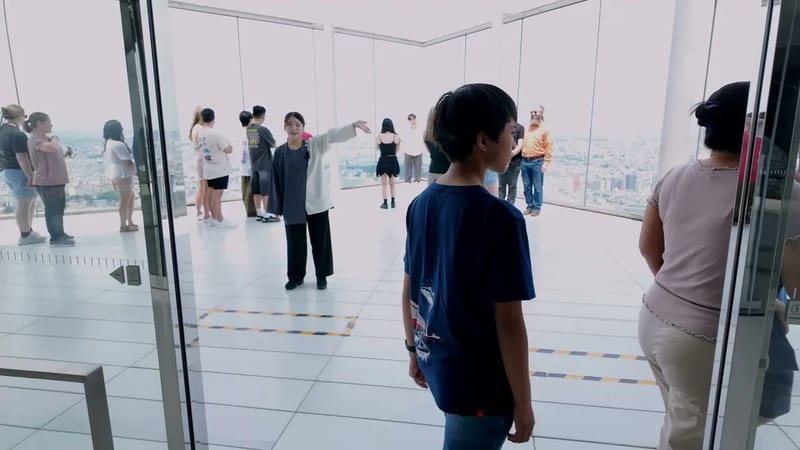 People inside the Shibuya Sky observation deck looking at the Tokyo, Japan city skyline through glass windows, a young boy in a blue shirt in the foreground.