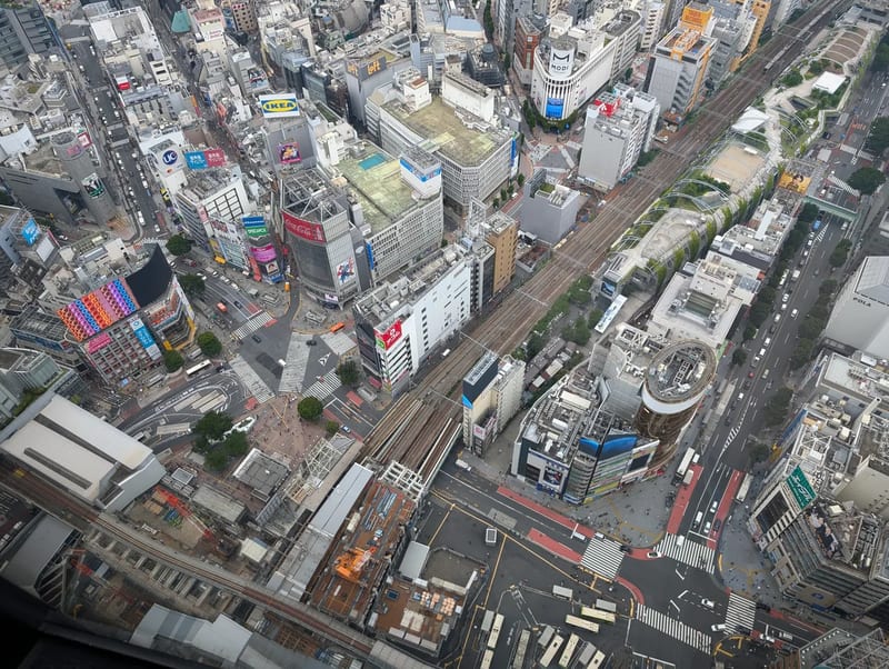 High-angle aerial view of dense Tokyo urban area from Shibuya Sky, showing buildings, complex road networks with traffic, and train tracks winding through the city, Shibuya, Tokyo, Japan.
