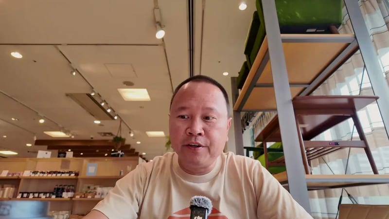Man in beige shirt and glasses seated in a cafe in Tokyo, Japan, speaking to camera.