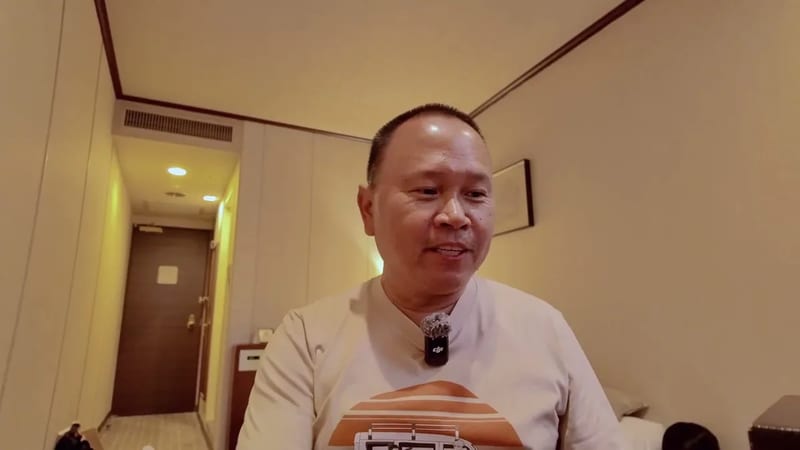 Man in beige shirt and glasses speaking to camera in a Tokyo hotel room, holding a Sony camera box, Tokyo, Japan.