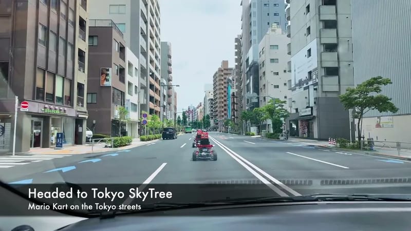 View from car of a Tokyo city street with go-karts from a Mario Kart street experience, buildings and blue road arrows visible.