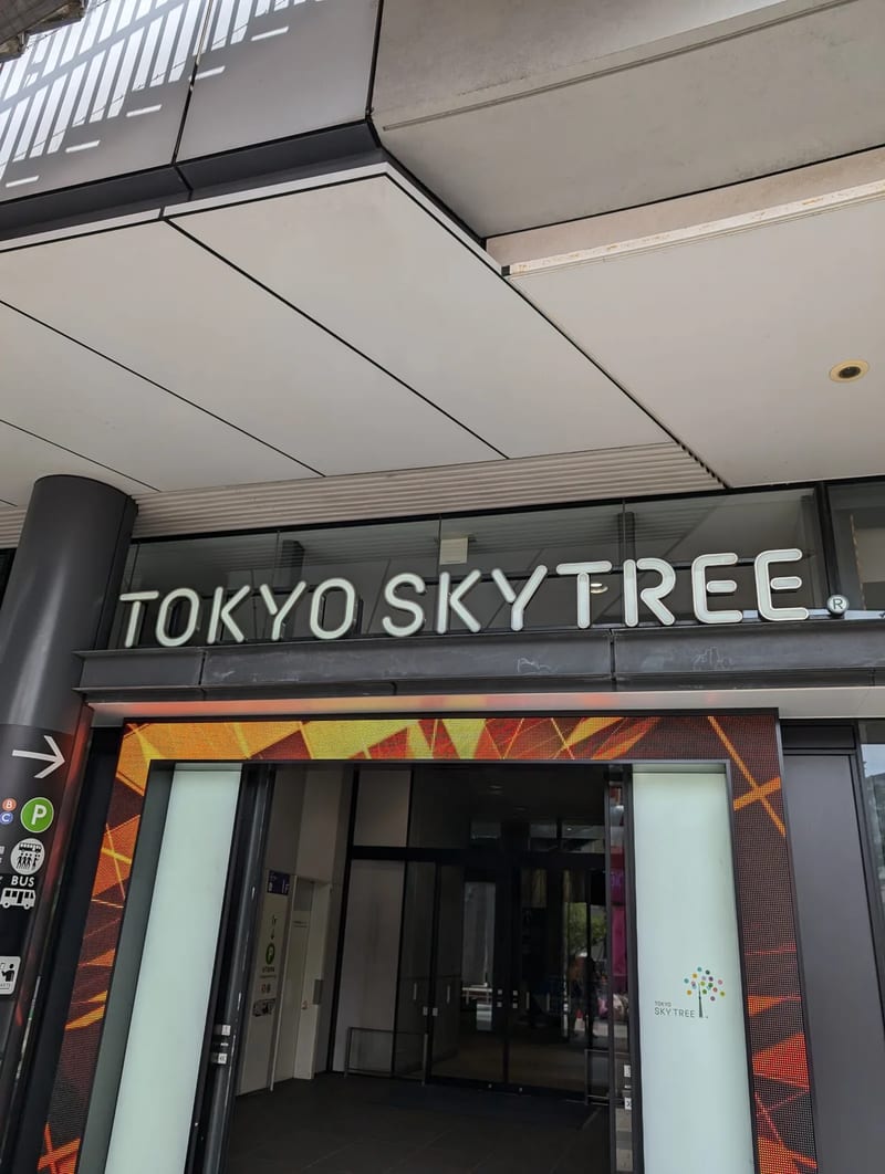 Entrance to the Tokyo Skytree complex with illuminated TOKYO SKYTREE sign and directional transport icons, Tokyo, Japan.