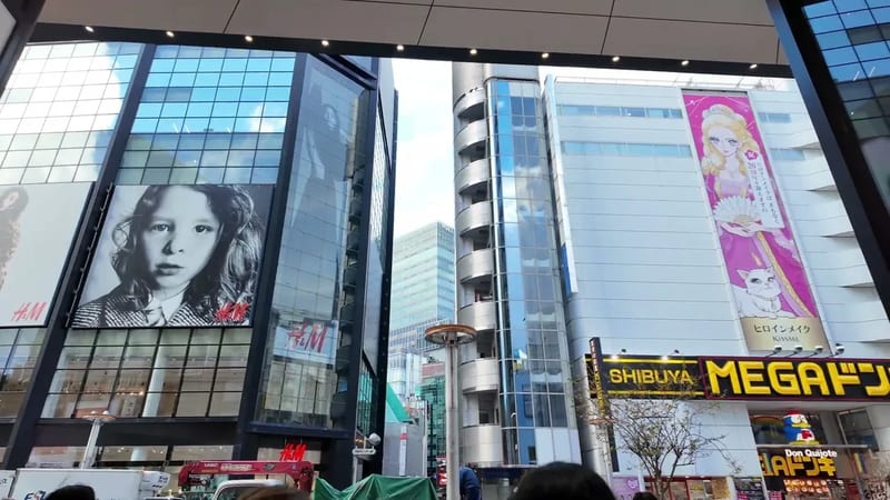 Street-level view of Shibuya with the Mega Don Quijote sign, H&M billboard, and anime advertisements on buildings in Tokyo, Japan