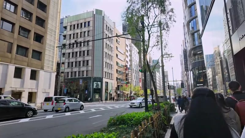 Wide shot of a bustling city street with modern buildings, cars, and pedestrians in Ginza, Tokyo, Japan.