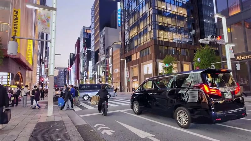 Busy city street at dusk with a black minivan and modern high-rise buildings in Ginza, Tokyo, Japan.
