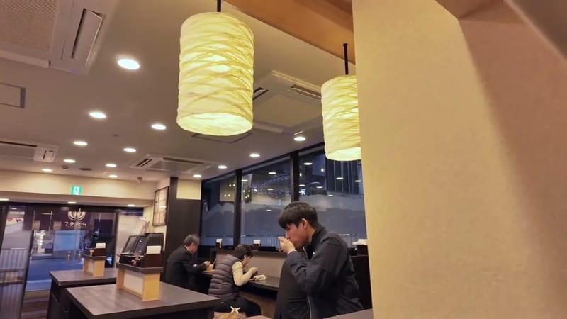 Man sipping from a cup at a brightly lit Japanese cafe with large paper lanterns in Ginza, Tokyo, Japan.